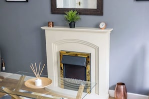 Una habitación con chimenea blanca, un reloj y una planta sobre la repisa.