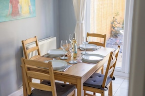 Una mesa de comedor dispuesta con platos, vasos y cubiertos, rodeada de sillas de madera con asientos acolchados.