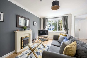 A living room with a fireplace, a television, a sofa, and a window with curtains. - Palma - Coastal Home near Harbour and beach (Poole)