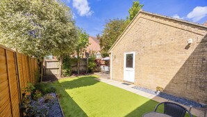 A backyard with a lawn, a brick building, a wooden fence, and a table with chairs. - Palma - Coastal Home near Harbour and beach (Poole)