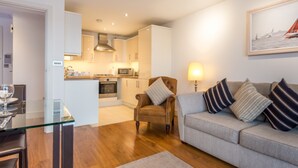 A modern living room with a glass dining table, a sofa with striped cushions, and a kitchen in the background. - Curlew - In the Heart of Poole Town (Poole)