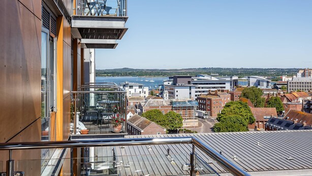 A high-rise building with a glass balcony overlooking a cityscape and water. - Curlew - In the Heart of Poole Town (Poole)
