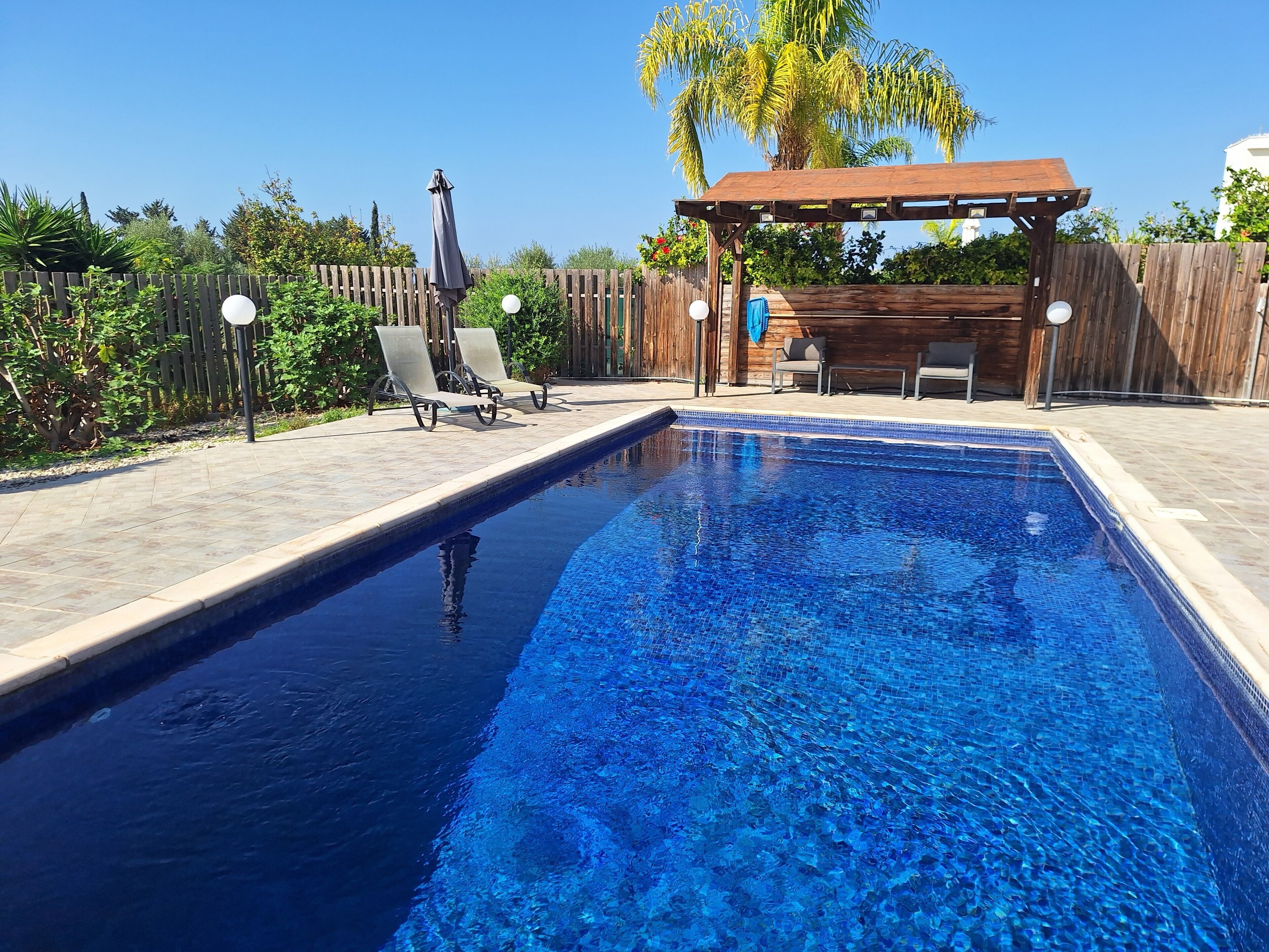 Una piscina rectangular con borde de azulejos, rodeada por una terraza de madera.