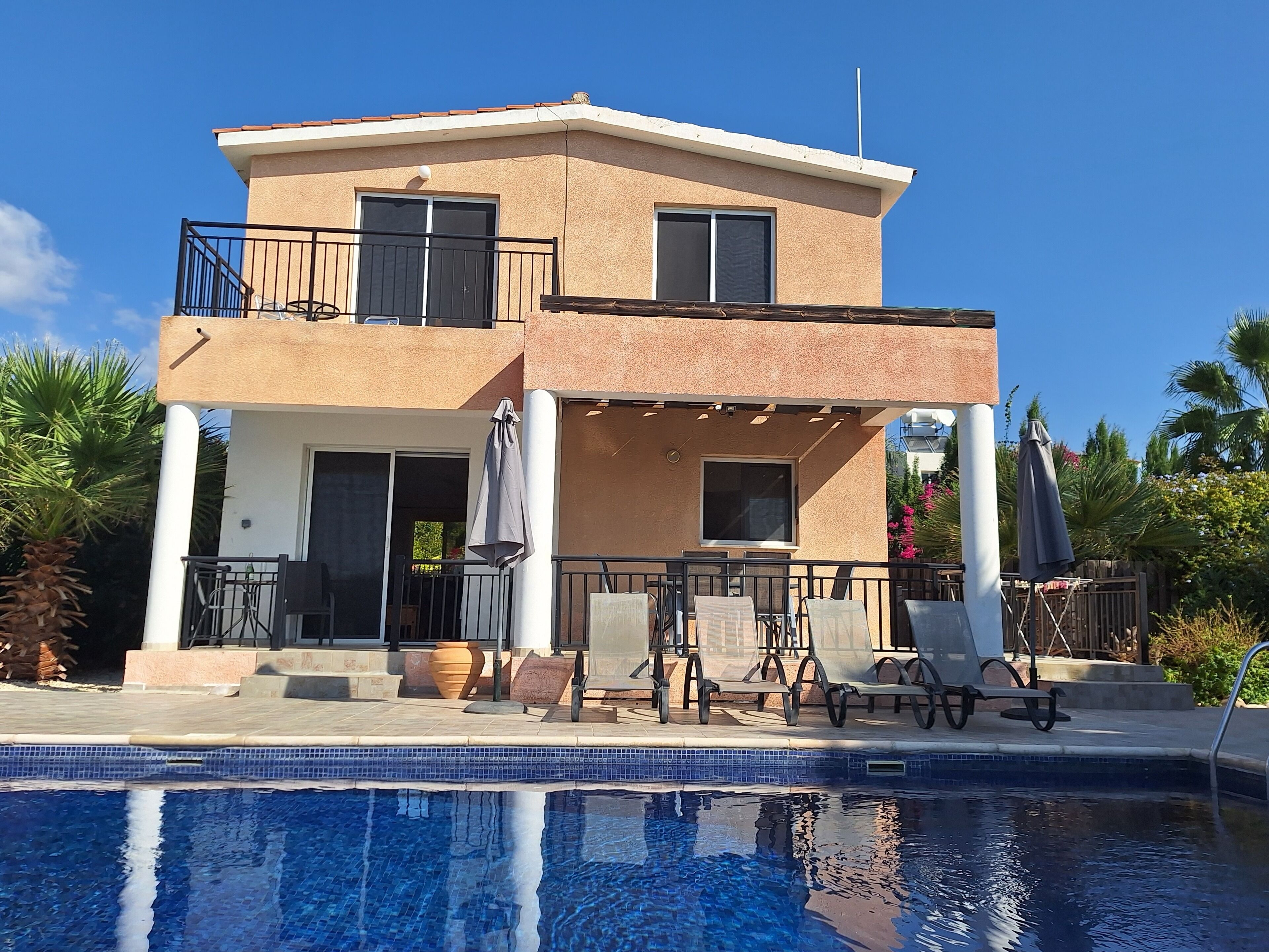 Un edificio a due piani con un balcone, una piscina e un'area salotto all'aperto.