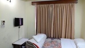 A hotel room with a bed, a TV mounted on the wall, and a window with curtains. - Hotel Dolphin (Kathmandu)