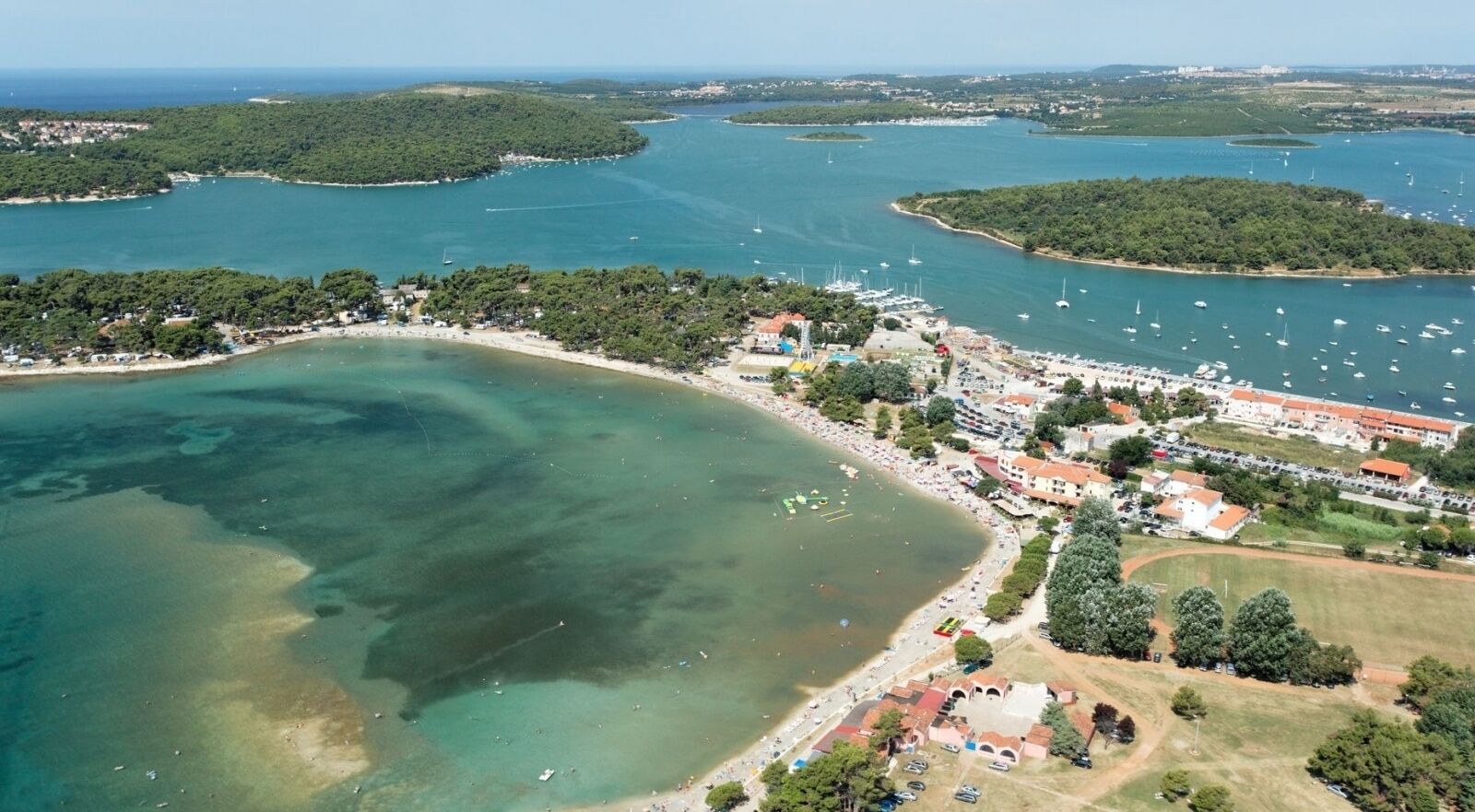 Eine Luftaufnahme einer Küstenstadt mit einem Yachthafen, Strand und Wohngebieten.