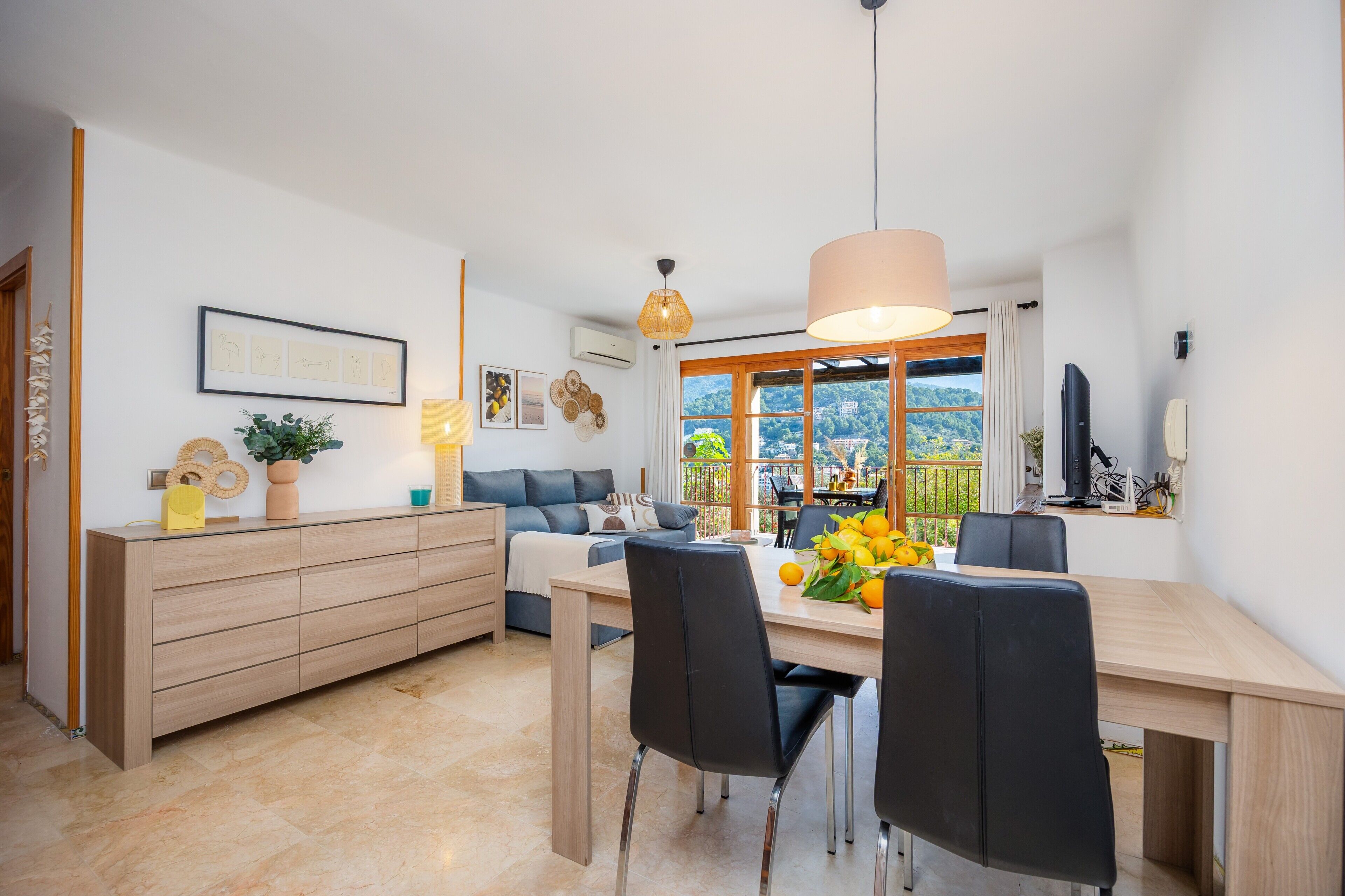Ein modernes Wohnzimmer mit einer Couch, einem Esstisch, Stühlen und Blick durch ein großes Fenster.