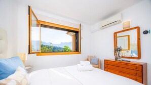 Un dormitorio con cama, cómoda, espejo, ventana y aire acondicionado.