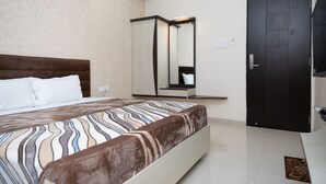 A hotel room with a bed, a dark door, a mirror, and a light switch on the wall. - Hotel Indian Heritage (Raipur)