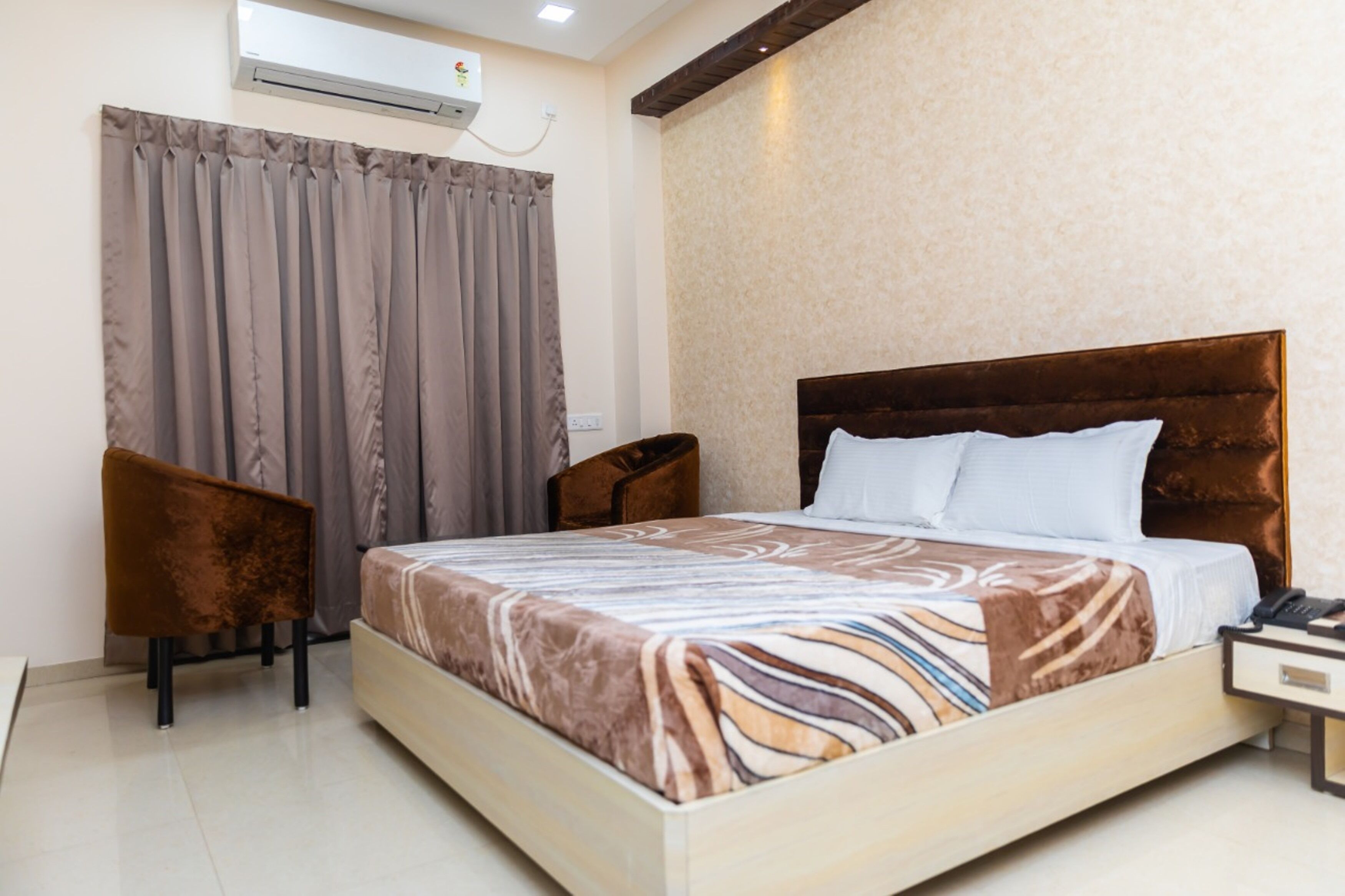 A hotel room with a bed, a chair, a nightstand, and an air conditioning unit.