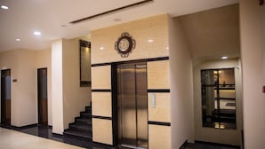 A modern hotel lobby with a central elevator, a staircase, and a reception area. - Hotel Indian Heritage (Raipur)
