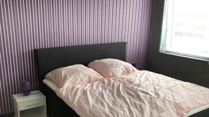 Ein Bett mit rosa Musterdecke, einem schwarzen Kopfteil und einem Nachttisch mit Lampe.