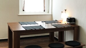 Ein Esstisch mit schwarzen Platzsets, eine Bank mit Kissen, ein Toaster und ein Fenster mit Vorhängen.