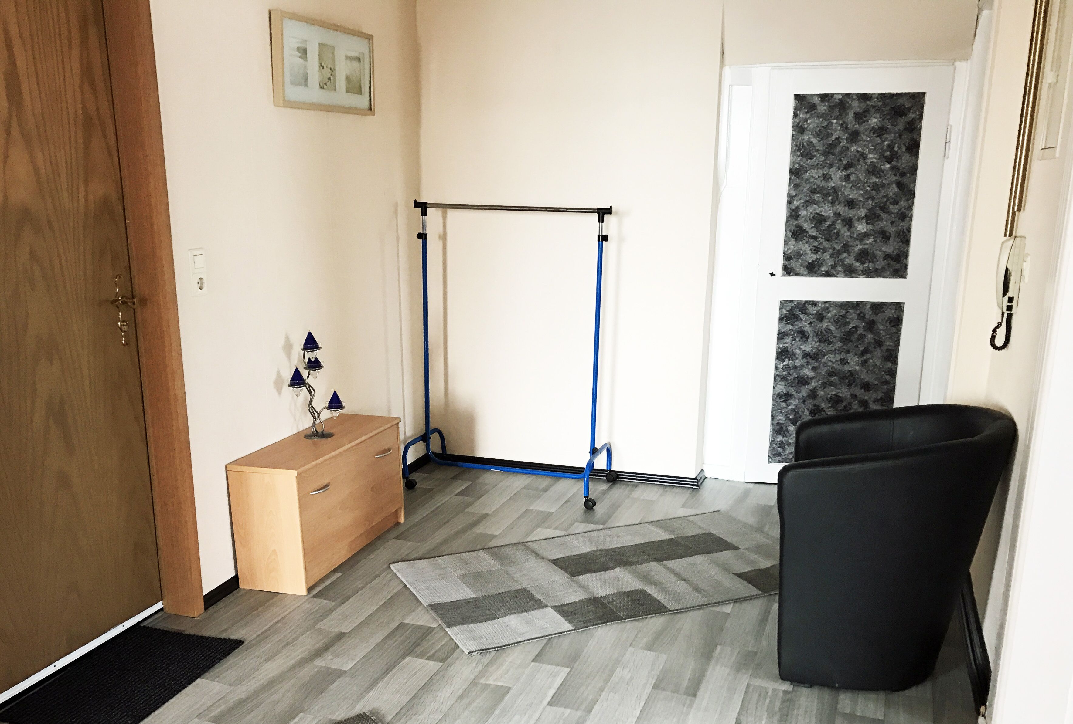 Une pièce avec une porte en bois, un bureau avec des tiroirs, une barre de gymnastique bleue, une chaise noire et un tapis à motifs.