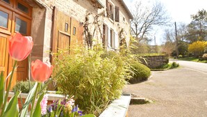 A stone building with wooden shutters, a garden with flowers, and a road in the background. - Small rustic cottage with terrace u. Hochgarten in outskirts (Tignécourt)