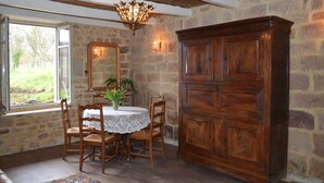 A dining area with a stone wall, wooden furniture, and a chandelier. - Small rustic cottage with terrace u. Hochgarten in outskirts (Tignécourt)