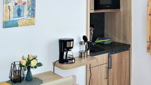A compact kitchen with wooden cabinets, a microwave, a coffee maker, and a small dining table with a chair. - Apartment 1 - House Erna (Bad Wildungen)