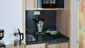 A compact kitchen with wooden cabinets, a Bosch microwave, a coffee maker, and a small countertop with a kettle and utensils. - Apartment 1 - House Erna (Bad Wildungen)