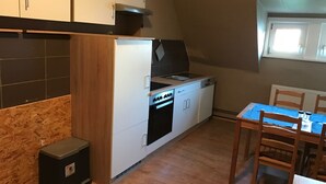 Ett kompakt kök med spis, ugn och diskho, träskåp och ett matbord med stolar.