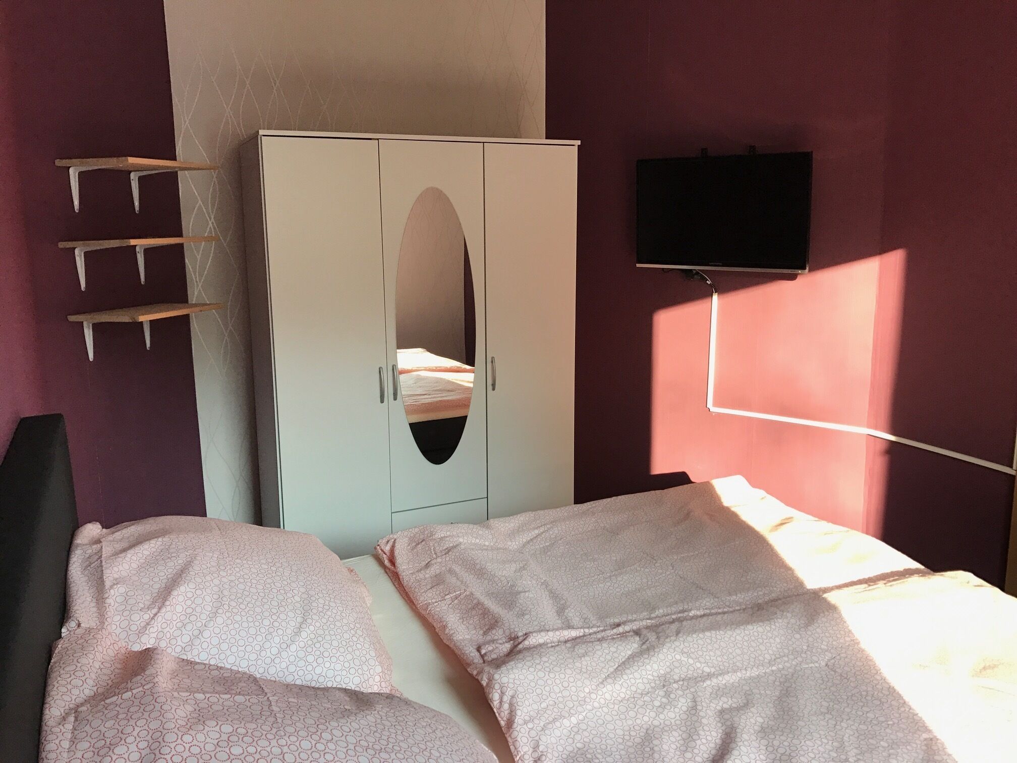 A bedroom with a bed, a wardrobe, and a TV mounted on the wall.