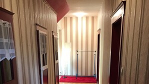 En hall med randiga tapeter, en röd matta och en dörr längst ner.