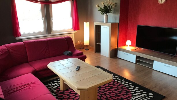 Ett modernt vardagsrum med en röd soffa, ett soffbord, en tv och en röd vägg med en klocka.