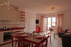 A dining area with a table set for four, a kitchen with modern appliances, and a living area with a sofa and curtains. - Atico La Plaza, Spain (Los Llanos)