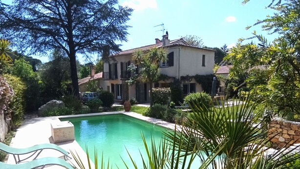 A pool surrounded by lush greenery and a house with a tiled roof.