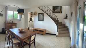 A dining area with a wooden table and chairs, a stone wall, a staircase with a decorative railing, and a window with curtains.