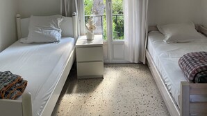 A bedroom with two single beds, a small bedside table with a lamp, and a window with curtains.