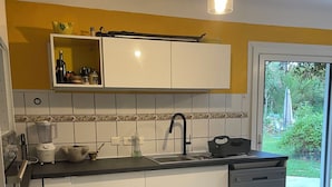 A kitchen with white cabinets, a black countertop, a patterned tile floor, and a view of a garden through a sliding glass door.