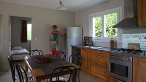 A compact kitchen with a refrigerator, oven, and a window with a view of greenery. - Domaine du Vernadel, Panoramic, swimming pool near Antraiques and Vals les Bains (Asperjoc)