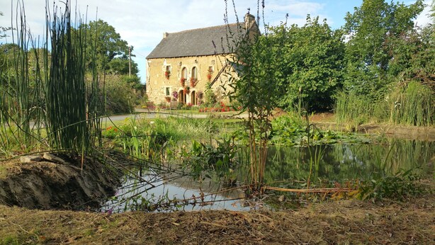 Een gebouw van steen met boogvensters en een tuin met een vijver.