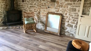 Ein rustikaler Raum mit Steinwand, Holzboden, einem Korbstuhl mit Kissen, einem Spiegel und einem Kamin.