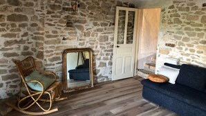 Ein Zimmer mit Steinwänden, einem Holzschaukelstuhl, einem Spiegel, einer weißen Tür und einem dunkelblauen Sofa.