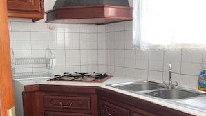 Una cocina con armarios de madera, estufa a gas, lavabo y una ventana con cortinas de encaje.