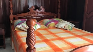 Una cama de madera con colcha a cuadros, cabecero con detalles tallados y mesita de noche con lámpara.