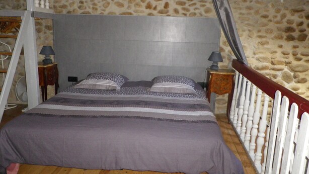 A bedroom with a stone wall, a wooden floor, a bed with patterned bedding, and a white railing.