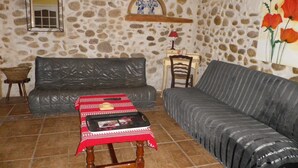 A cozy living room with a stone wall, a black leather sofa, a red and white patterned table, and a wooden chair.