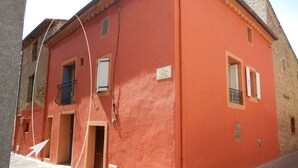 A red building with a balcony, a door, and a window with shutters.