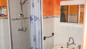 A bathroom with a glass shower enclosure, a white sink, and an orange wall.