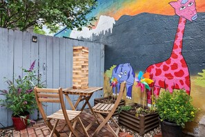 Ein Holztisch und Stühle in einer Gartenanlage mit einer farbenfrohen Wandmalerei, die eine Giraffe und einen Elefanten zeigt.