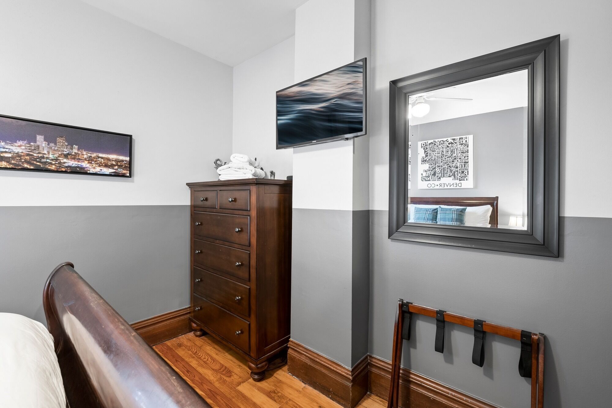 Une chambre à coucher avec un lit, une commode, un miroir et des œuvres d’art accrochées aux murs.
