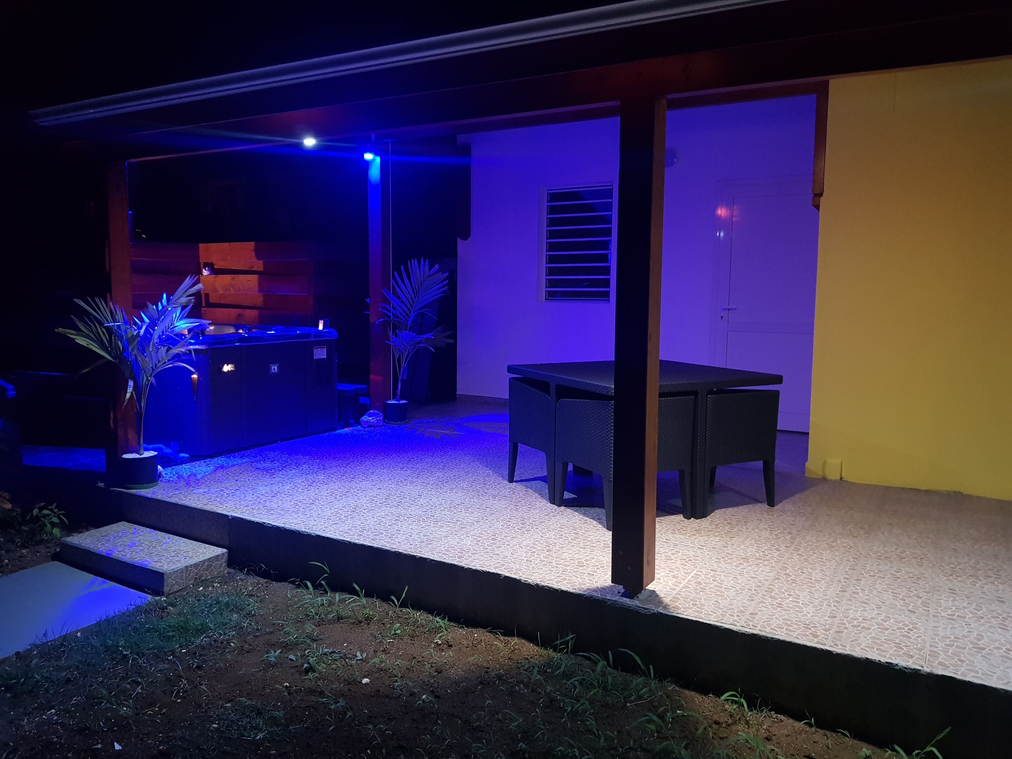Un espace extérieur aménagé en patio, avec une table et des chaises, un petit coin cuisine doté d’un comptoir et d’un évier, ainsi que des plantes en pot.