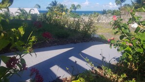 A garden with various plants and flowers, a paved area, and a view of the ocean. - COZY COTTAGE + NETFLIX + WIFI + JACCUZZI + PARKING (Sainte rose)