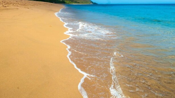 A beach with clear blue water, a sandy shore, and a distant hill. - COZY COTTAGE + NETFLIX + WIFI + JACCUZZI + PARKING (Sainte rose)