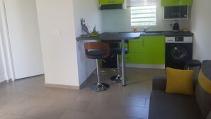 A compact kitchen with a washing machine, a dining area with a bar stool, and a living area with a sofa. - COZY COTTAGE + NETFLIX + WIFI + JACCUZZI + PARKING (Sainte rose)