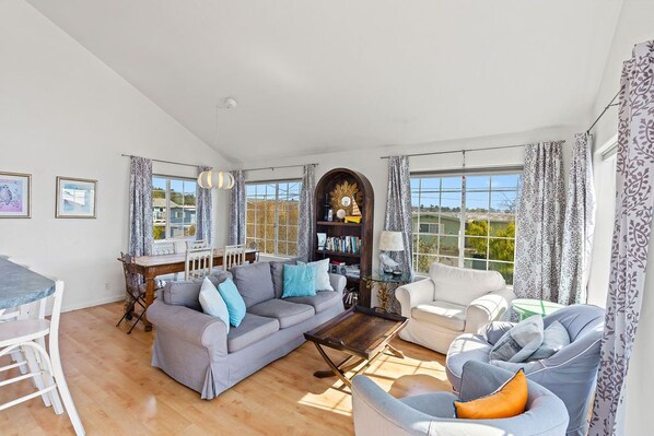 A spacious living room with a grey sofa, a white armchair, and a dining area with a table and chairs. - Charming, Sunny Home! (Aptos)