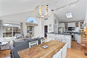 A spacious living area with a wooden dining table, grey sofas, and a kitchen with white cabinets and modern appliances. - Charming, Sunny Home! (Aptos)