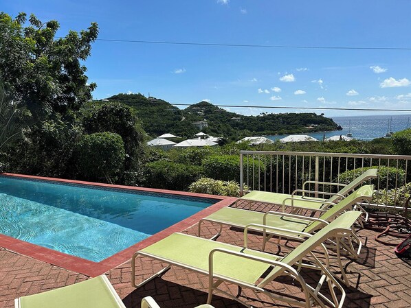 Une piscine avec des chaises longues et une vue sur la mer et les collines.